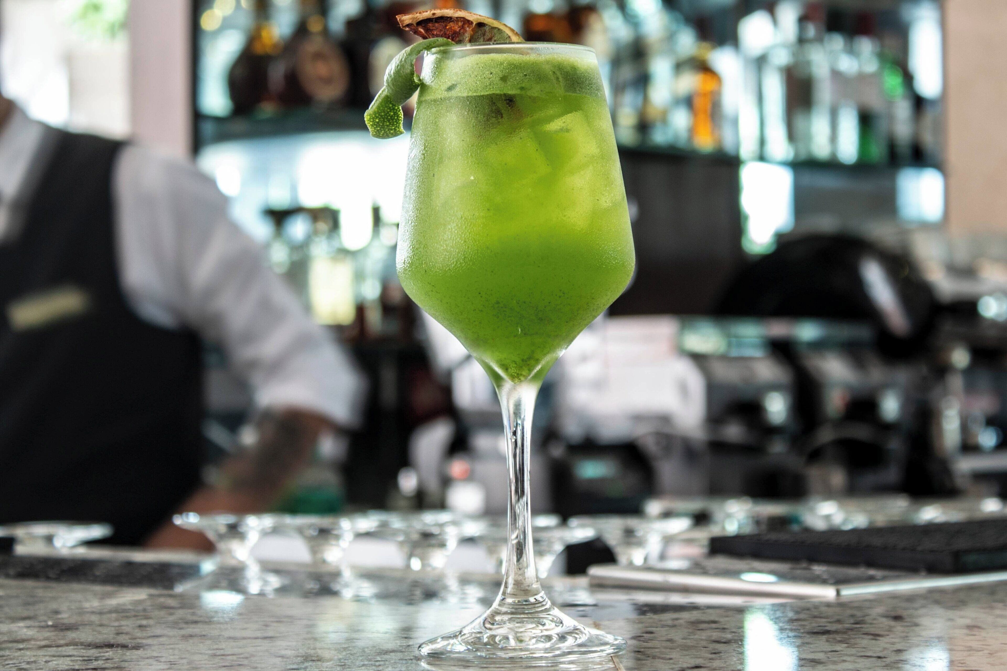 Un cóctel verde en una copa de martini sobre la barra.