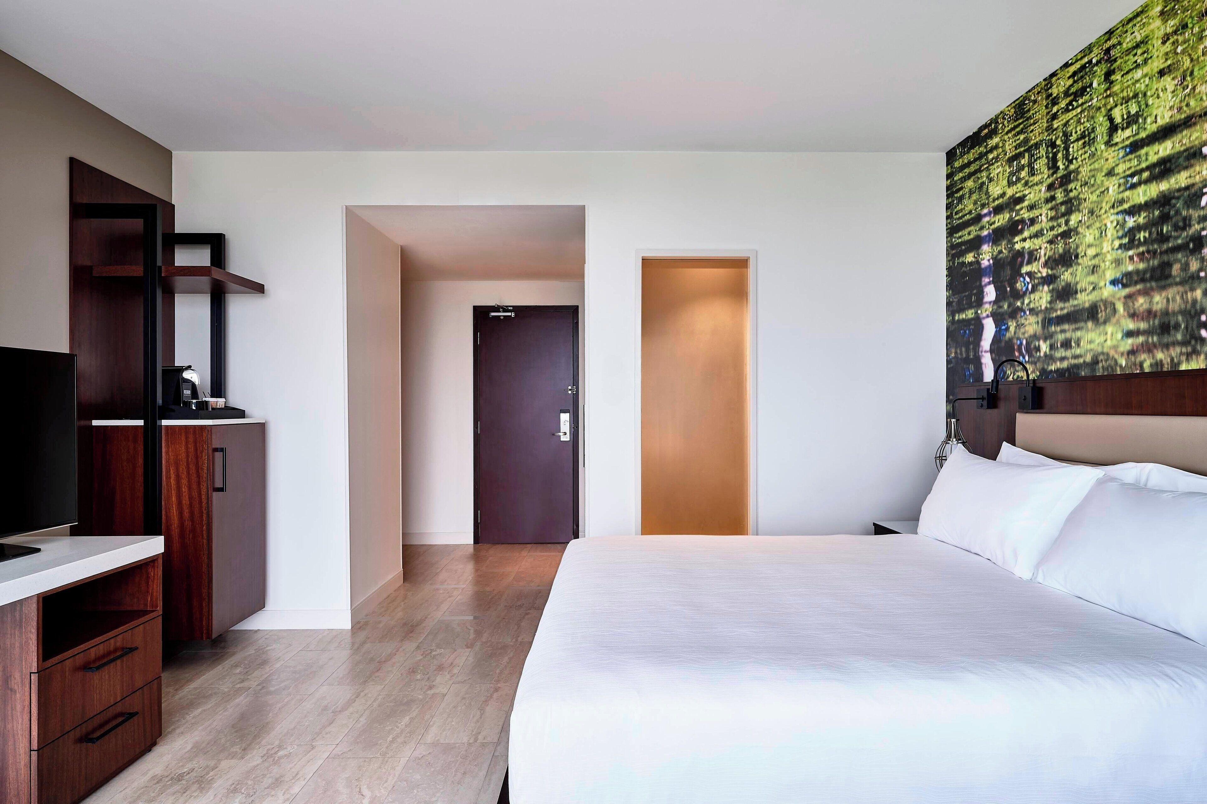 Ein Hotelzimmer mit einem großen Bett, einem Fernseher, einem Holzschrank und einer Tür zu einem weiteren Raum.