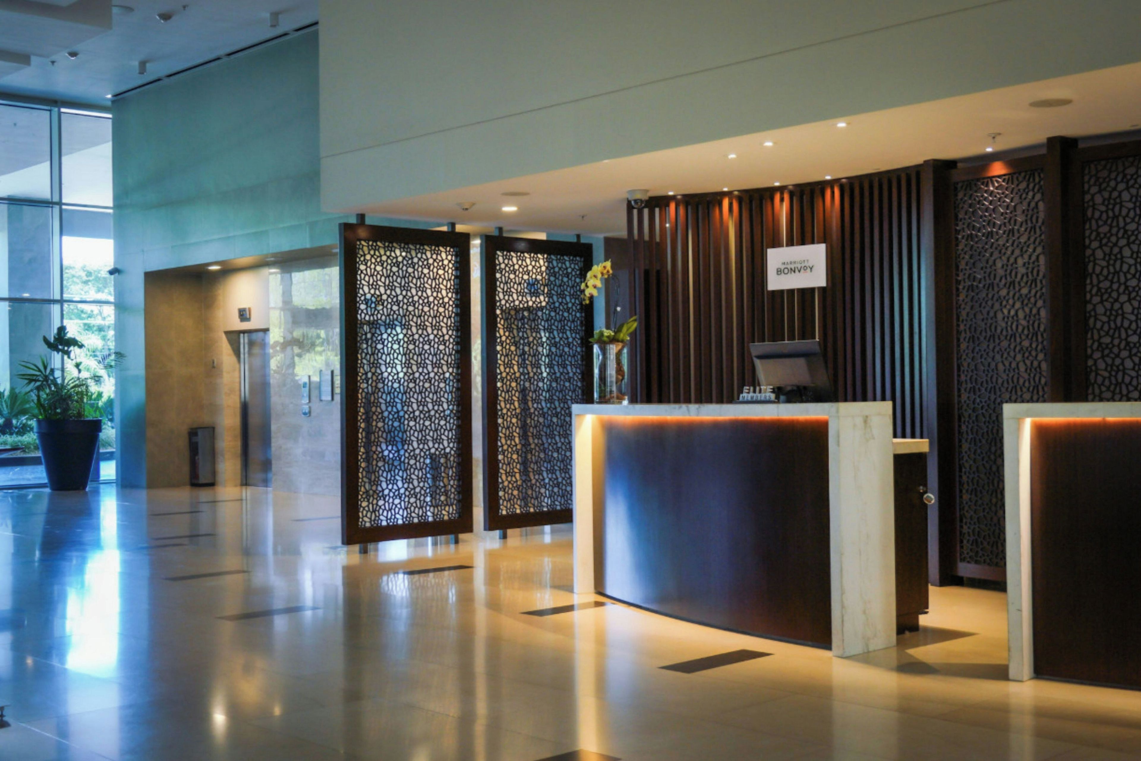 A modern hotel reception area with a glass partition, a reception desk, and a sign indicating the hotel name.