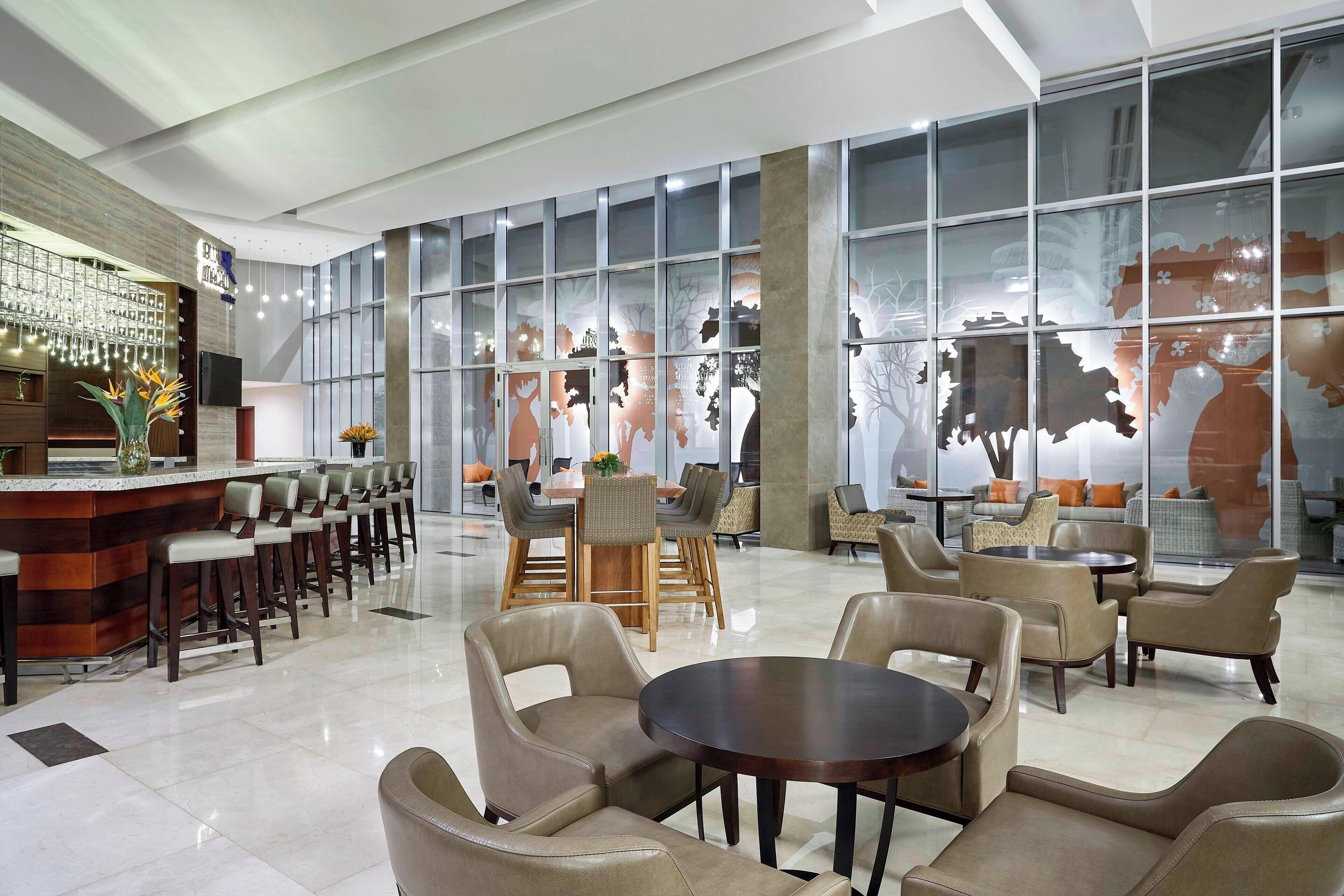 A modern hotel lobby with a bar area, seating arrangements, and large windows.