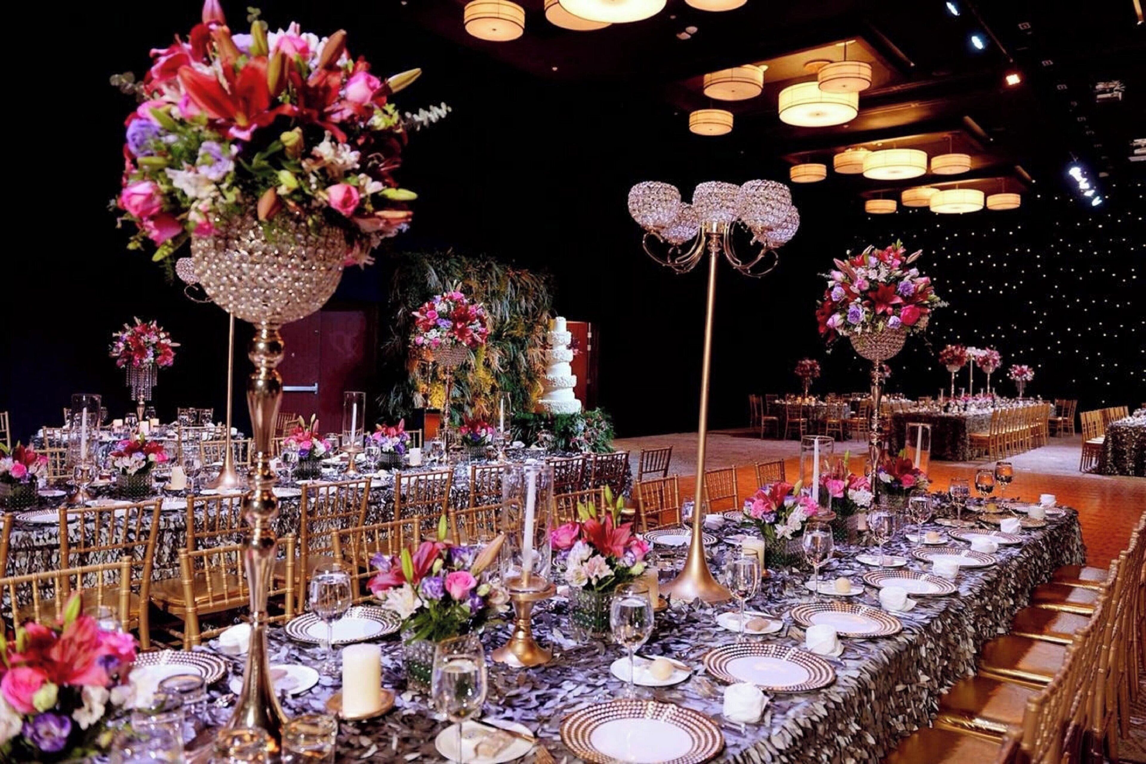 A banquet hall with long tables set for a formal event, featuring floral centerpieces and elegant tableware.