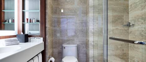 Un baño moderno con cabina de ducha de vidrio, inodoro blanco y tocador con espejo y estantes.