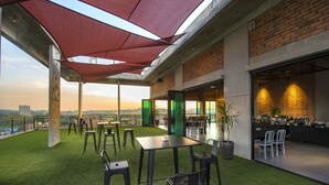 An outdoor terrace with artificial grass, tables, chairs, and a large umbrella. - Ibis Styles Kota Kinabalu Inanam Hotel (Kota Kinabalu)