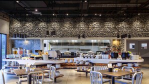 A modern cafeteria with multiple dining tables and chairs, a buffet area with various food items, and a kitchen in the background. - Ibis Styles Kota Kinabalu Inanam Hotel (Kota Kinabalu)