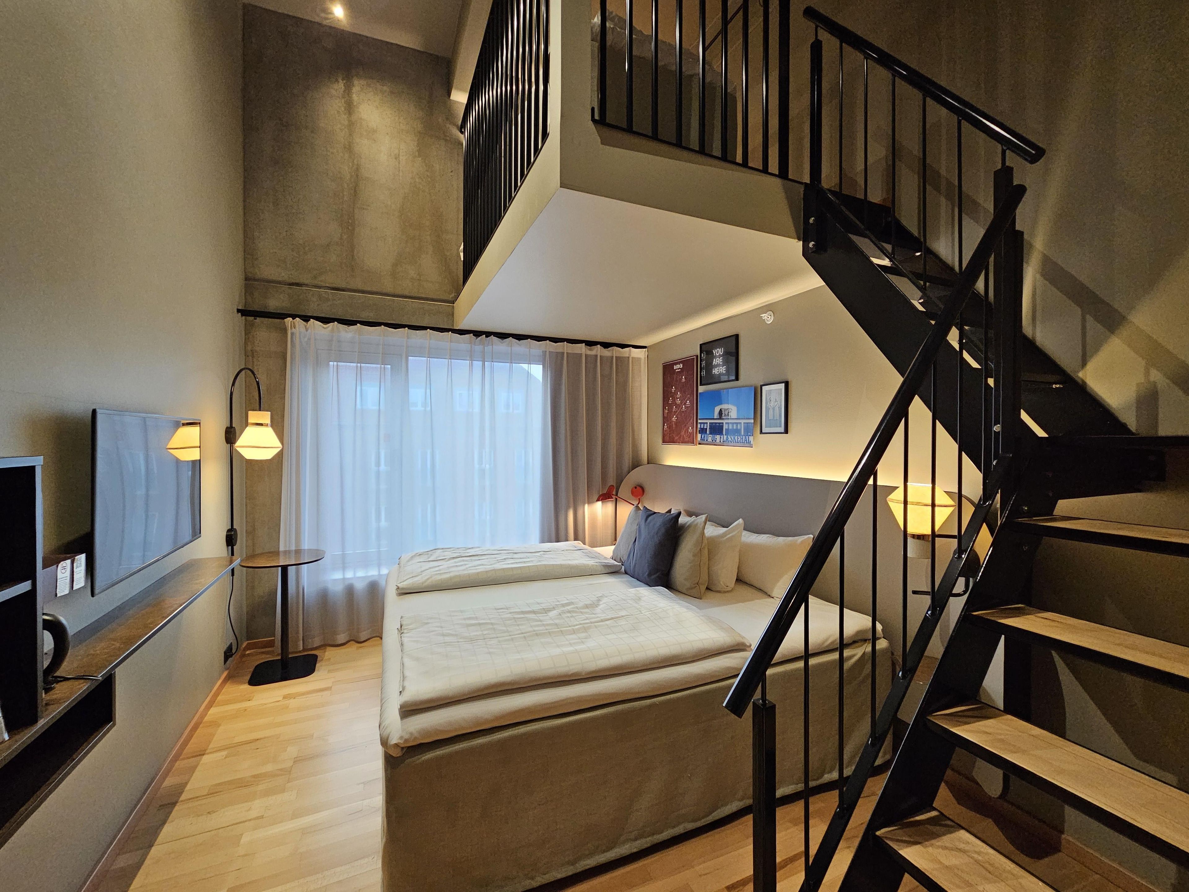 A bedroom with a bed, a TV, a desk, and a staircase.