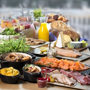 A breakfast buffet with various dishes including smoked salmon, ham, scrambled eggs, and a selection of breads and cheeses.