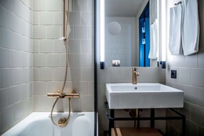 A modern bathroom with white tiles, a white sink, and a shower with a gold faucet.