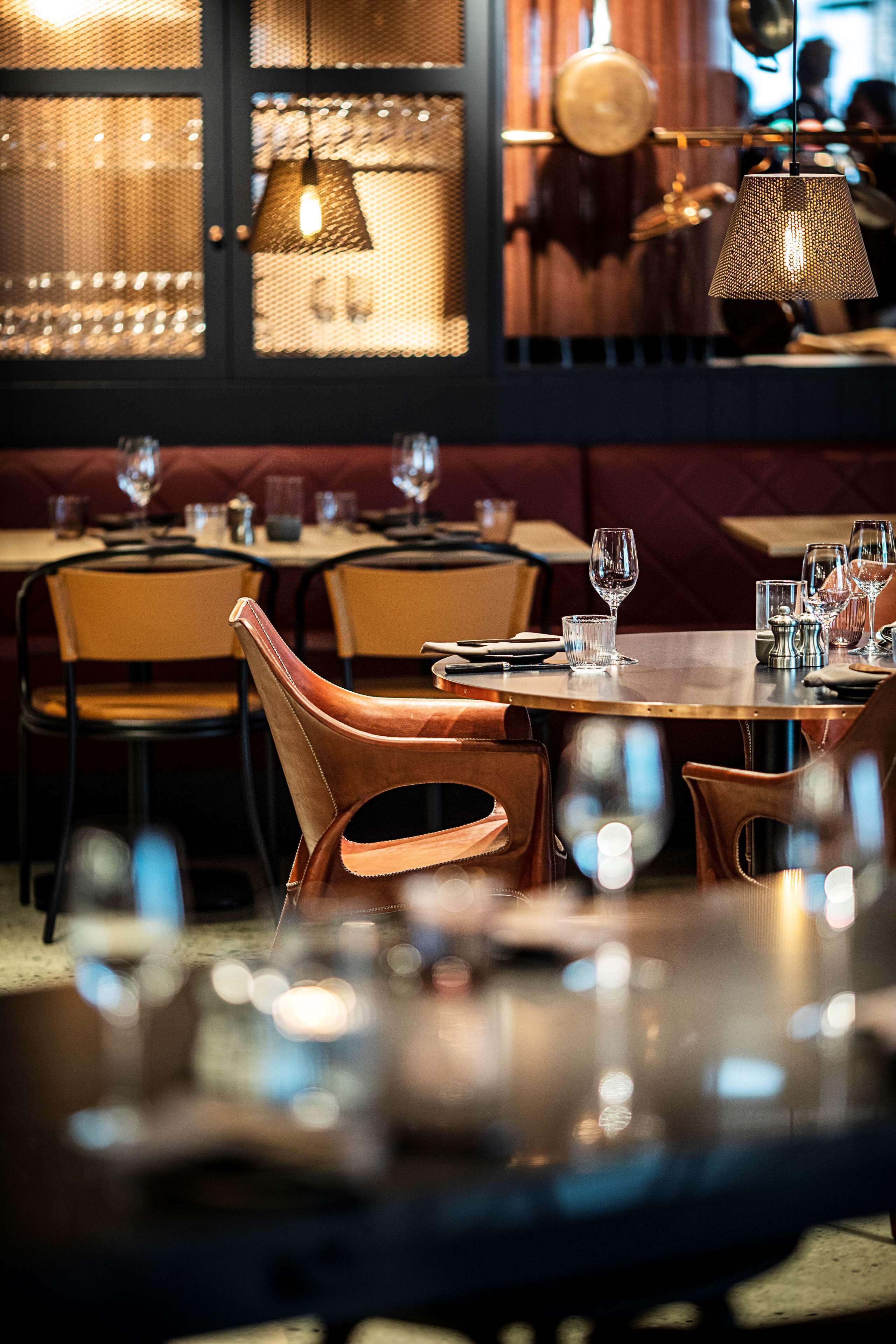 Ein Restaurantinneres mit runden Tischen, gepolsterten Stühlen und hängenden Pendelleuchten.