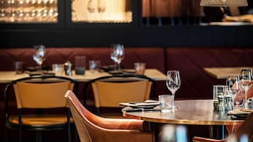Ein Restaurantinneres mit runden Tischen, gepolsterten Stühlen und hängenden Pendelleuchten.