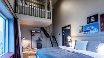 Habitación de hotel moderna con una cama grande, un escritorio, una silla, un armario y una escalera que lleva a un nivel superior.