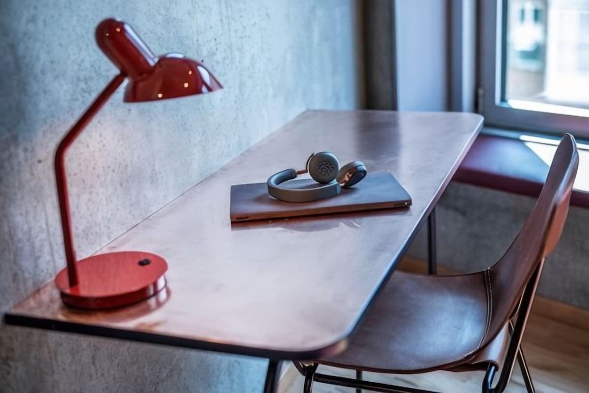 Una mesa con una lámpara de escritorio roja, auriculares y un cuaderno.