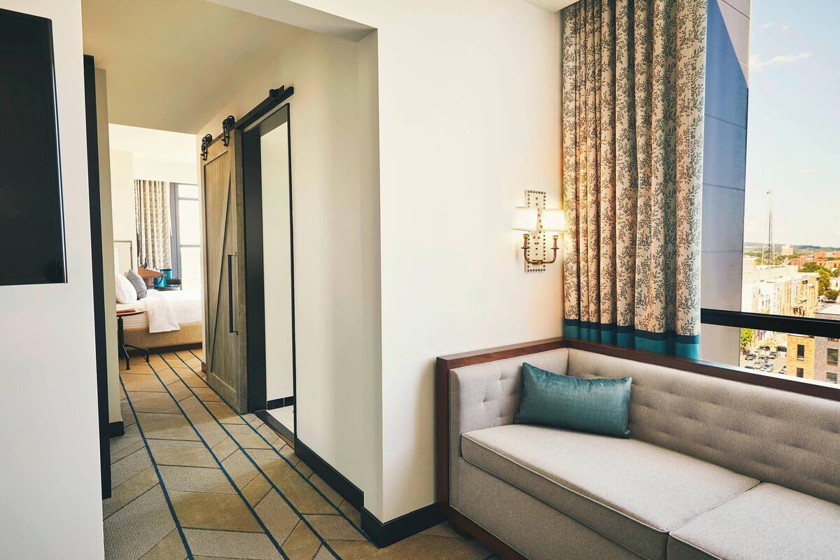 A hotel room with a sofa, a bed, a large mirror, and a view of the city through the window.