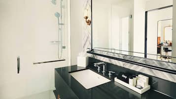 A modern bathroom with a glass shower enclosure, a black countertop, a white sink, and a large mirror.