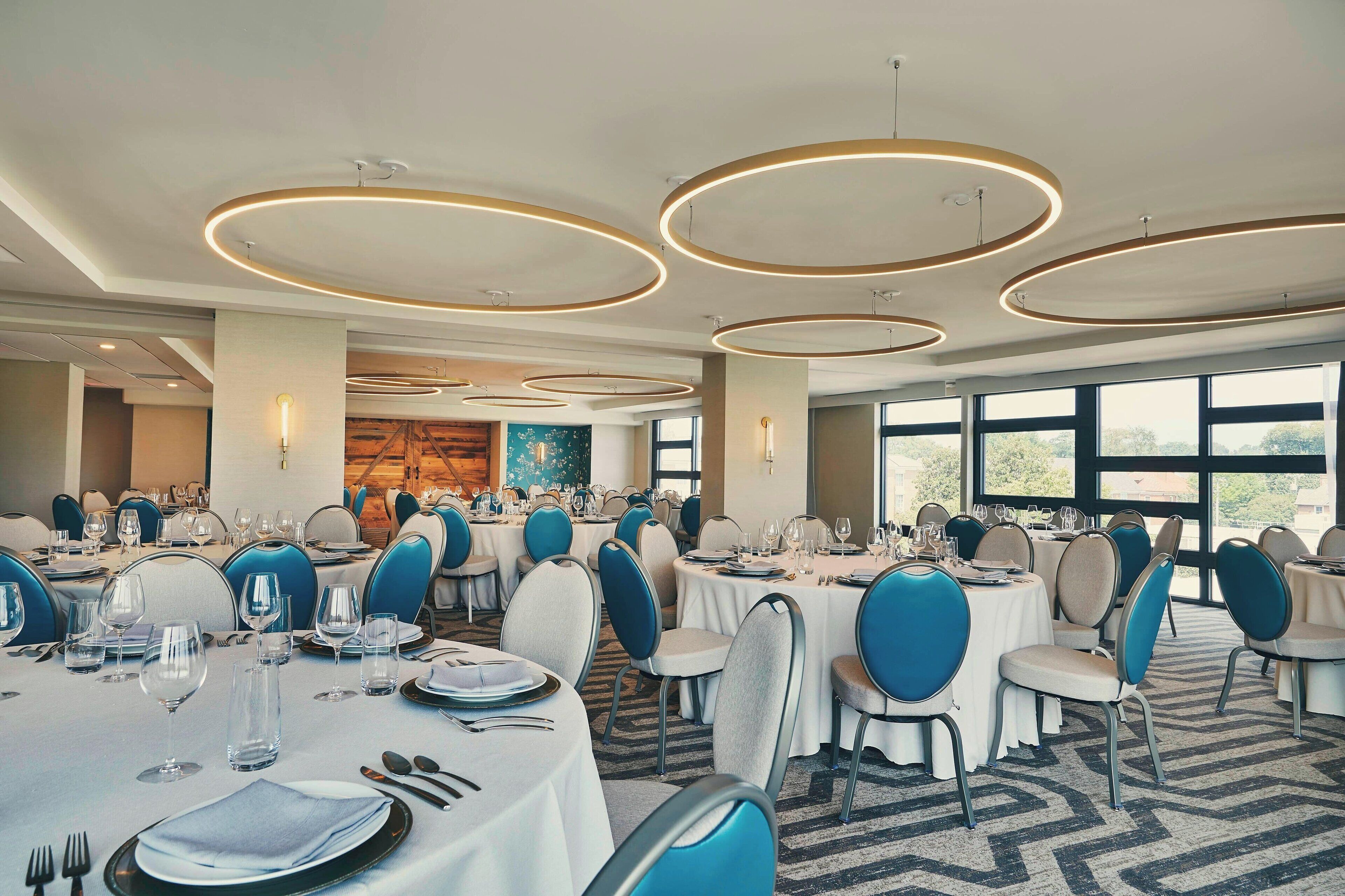 Un amplio salón de banquetes con mesas redondas, sillas azules y modernos accesorios de iluminación.