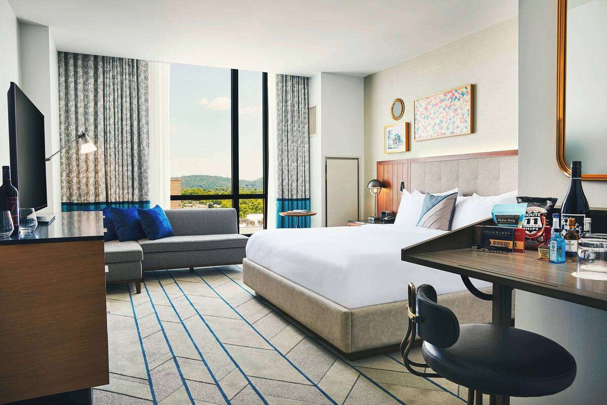 A hotel room with a large bed, a desk with a chair, a sofa, and a view of the outdoors.