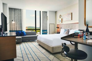 A hotel room with a large bed, a desk with a chair, a sofa, and a view of the outdoors.