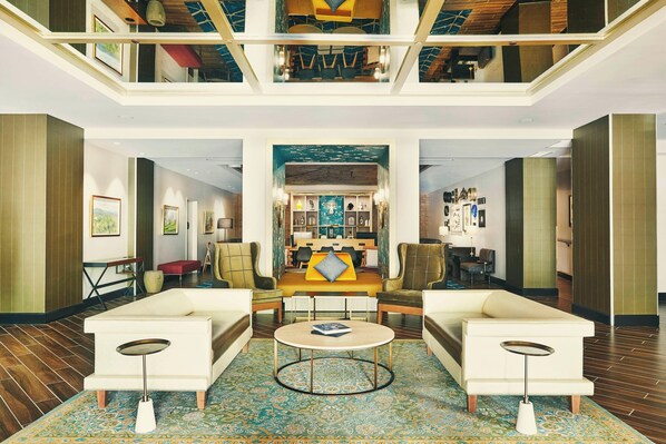 A spacious lobby with a high ceiling, a central seating area with sofas and a coffee table, and a view of the upper floor.