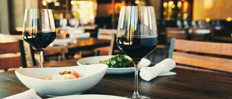 A restaurant setting with a wooden table, two wine glasses, and plates of food.
