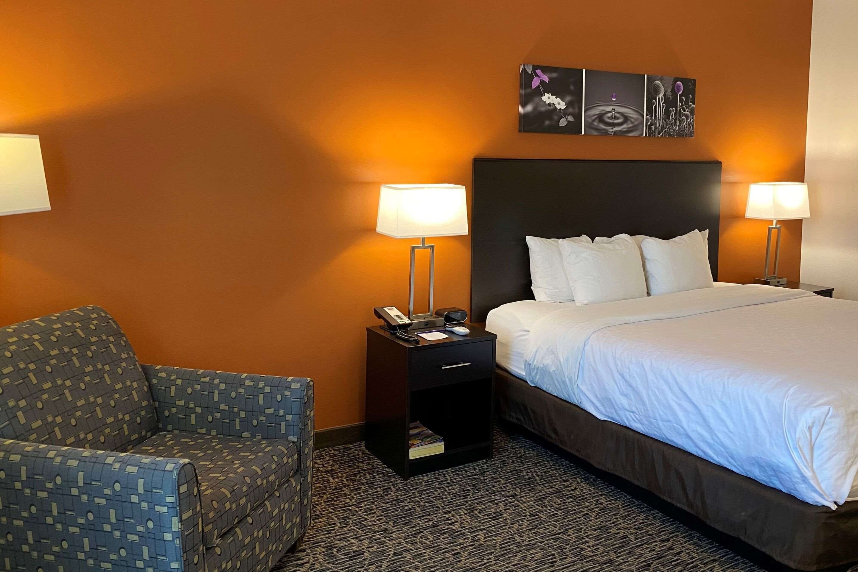 Une chambre d’hôtel comprenant un lit, deux tables de chevet avec des lampes, une chaise et une œuvre d’art accrochée au mur.