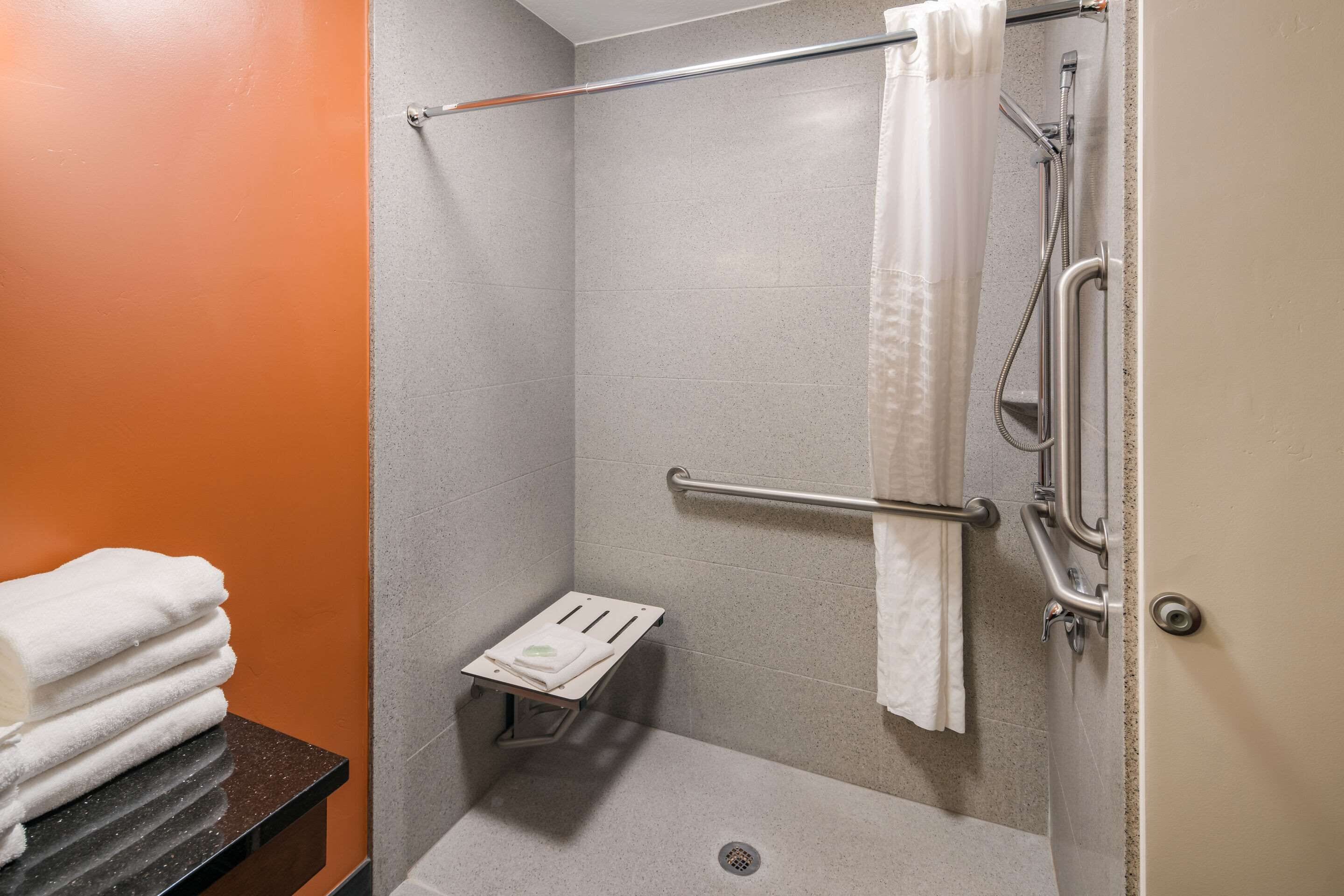A shower area with a grab bar, a small bench, and a towel rack.
