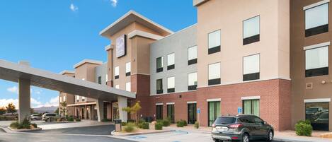 A multi-story hotel with a modern design, featuring a parking lot and a covered walkway.