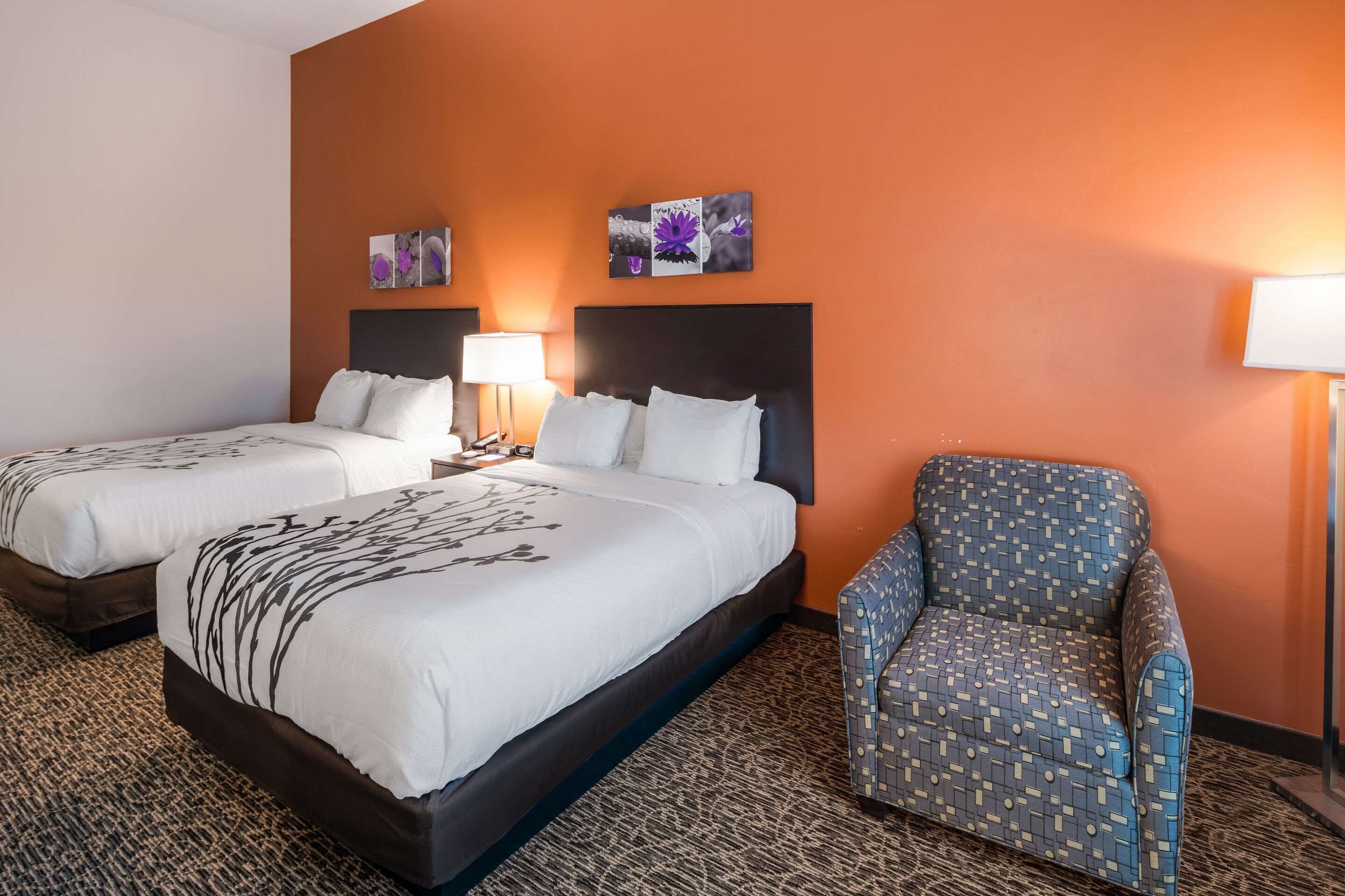 A hotel room with two beds, a patterned armchair, and artwork on the walls.