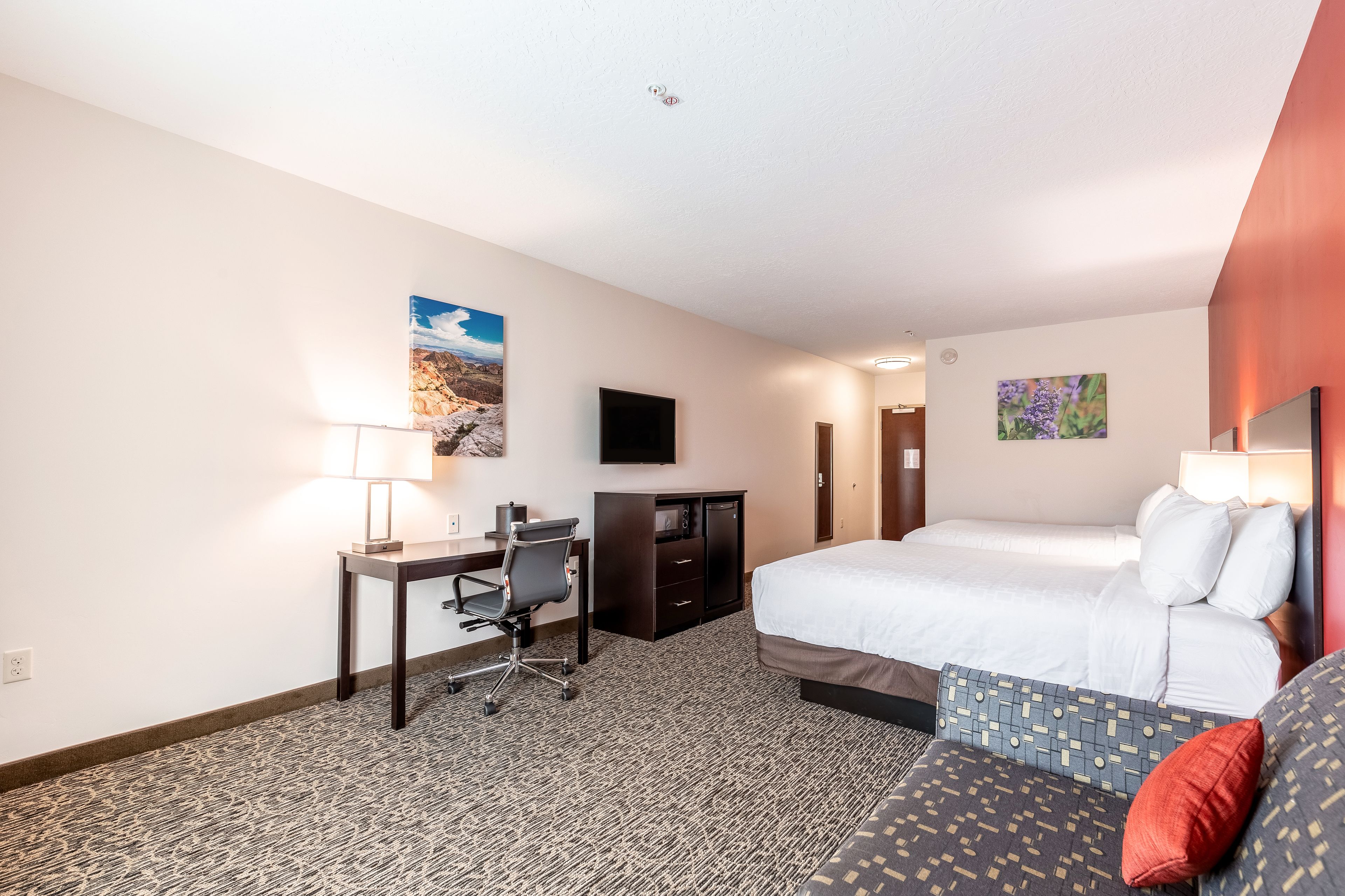 Een hotelkamer met een bed, bureau, stoel, televisie en kunstwerken aan de muur.