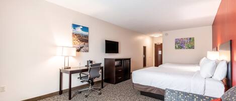 A hotel room with a bed, desk, chair, TV, and artwork on the walls.