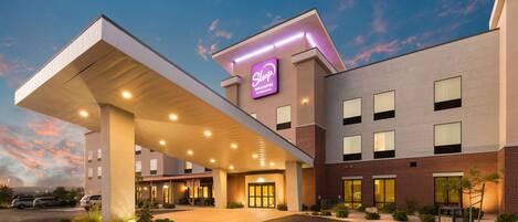 A hotel with a modern design, featuring a prominent neon sign, a covered parking area, and a well-lit entrance.