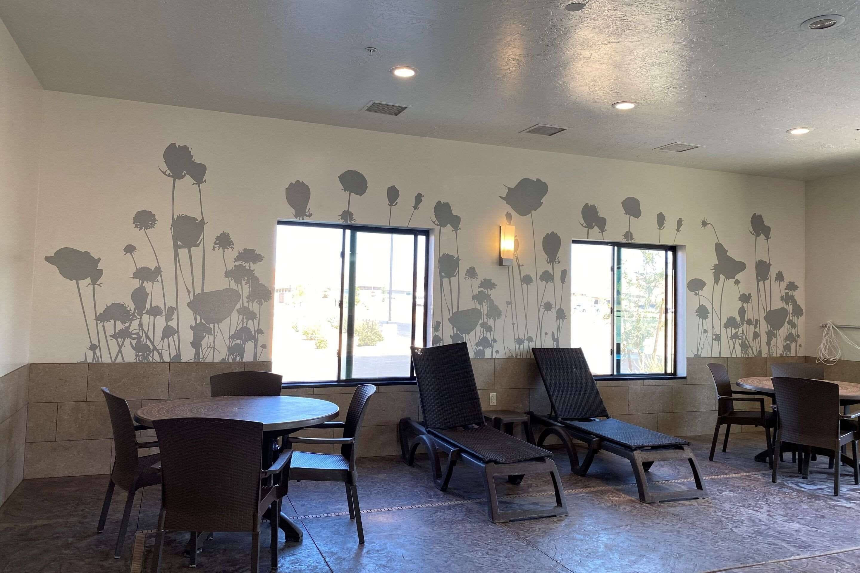 A dining area with a round table and chairs, a sun lounger, and a wall with a floral mural.