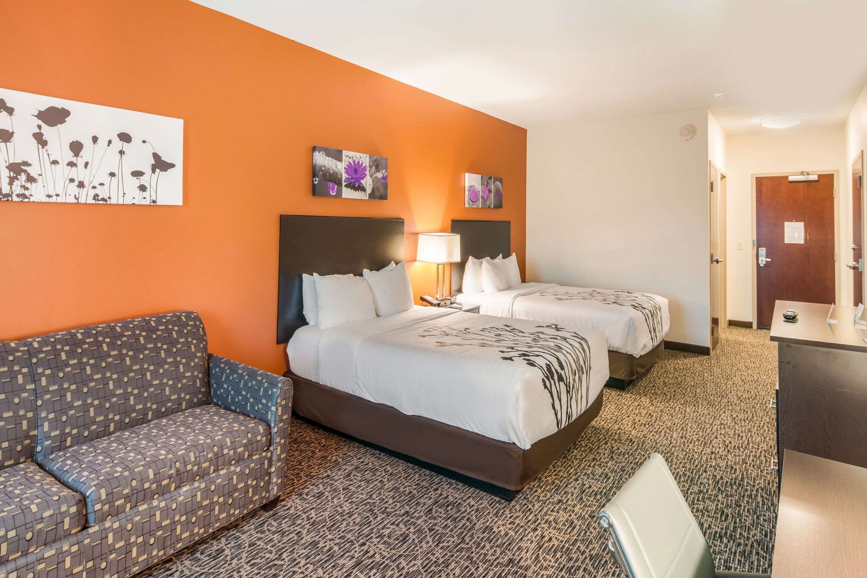 A hotel room with two beds, a sofa, a desk, and artwork on the walls.
