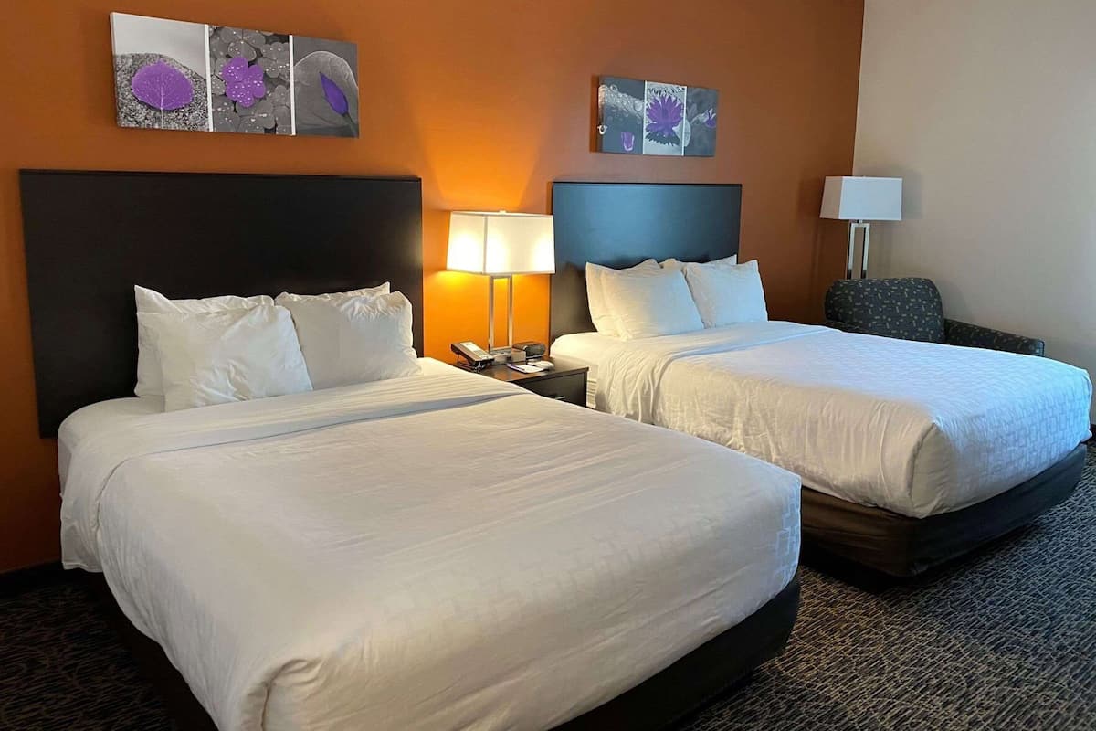 Una habitación de hotel con dos camas, una mesita de noche, una lámpara y obras de arte en las paredes.