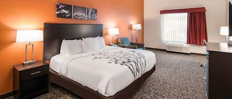 A hotel room with a large bed, two bedside tables with lamps, a chair, a desk, and a TV.