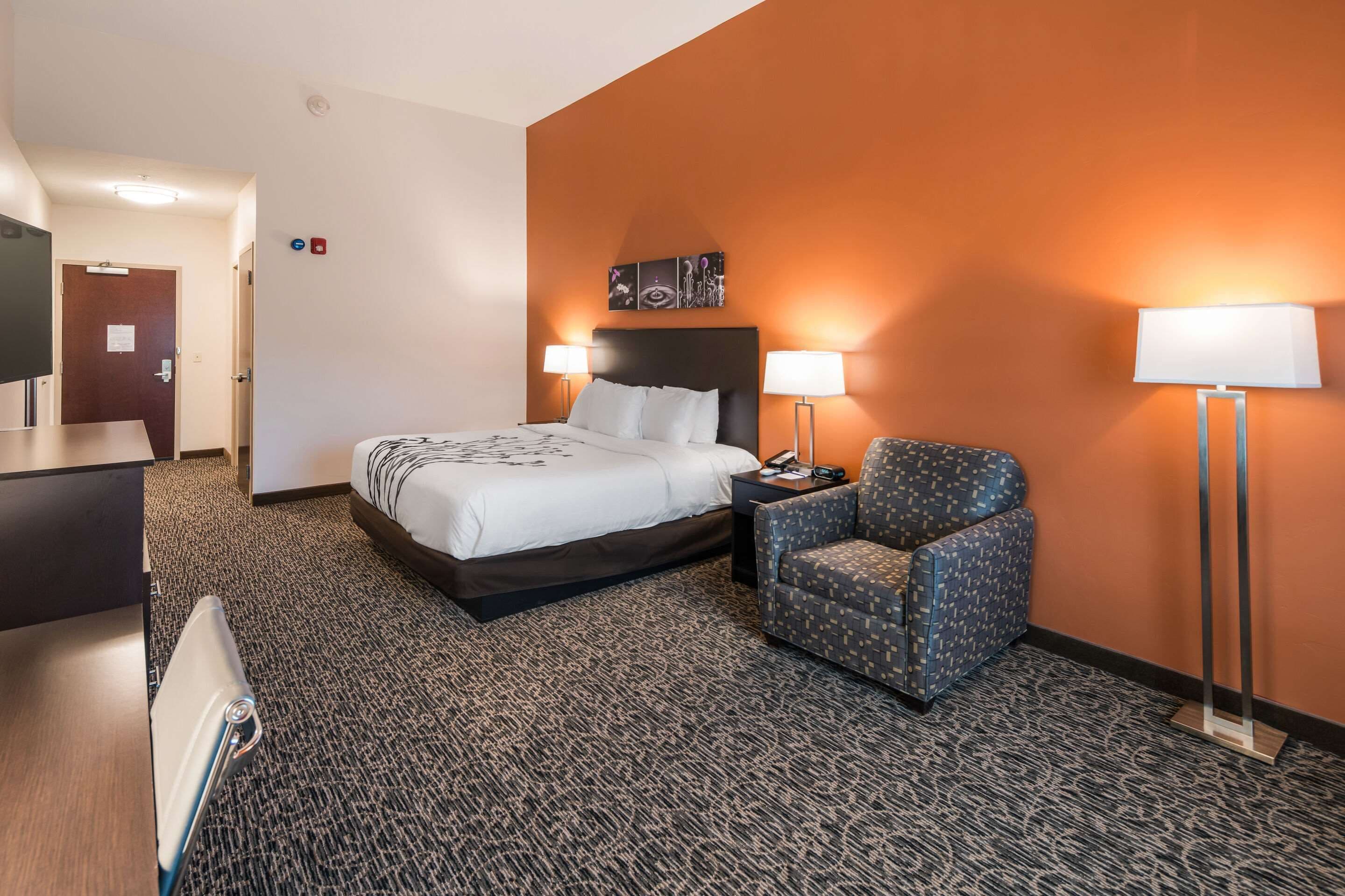 A hotel room with a bed, two bedside lamps, a chair, a desk, and a flat-screen TV.