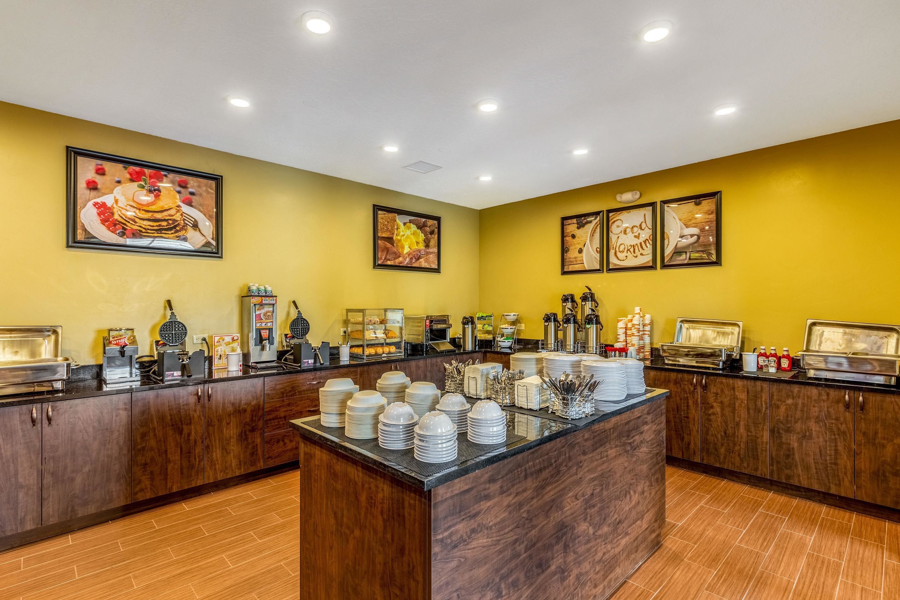 A buffet setup with multiple food stations, a central serving area with stacked plates, and wall-mounted artwork depicting food items.