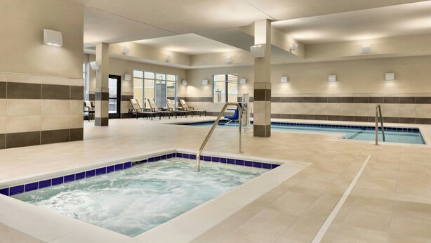 A large indoor swimming pool with multiple lanes, a separate hot tub area, and lounge chairs along the poolside.
