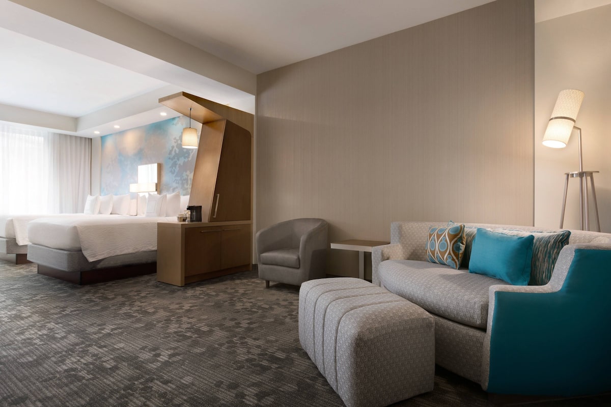 A hotel room with a bed, a sofa, a chair, a small table, and a lamp.