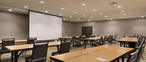 A conference room with multiple tables and chairs, a projector screen, and a carpeted floor.