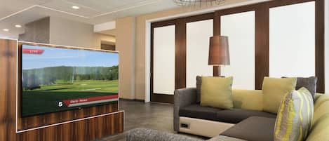 Una sala de estar moderna con un televisor de pantalla plana mostrando un campo de golf, un sofá y una lámpara.