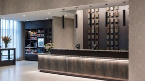 Un espace d’accueil moderne avec un comptoir en marbre, un panneau mural présentant différentes textures évoquant la pierre, et une bibliothèque contenant divers objets.