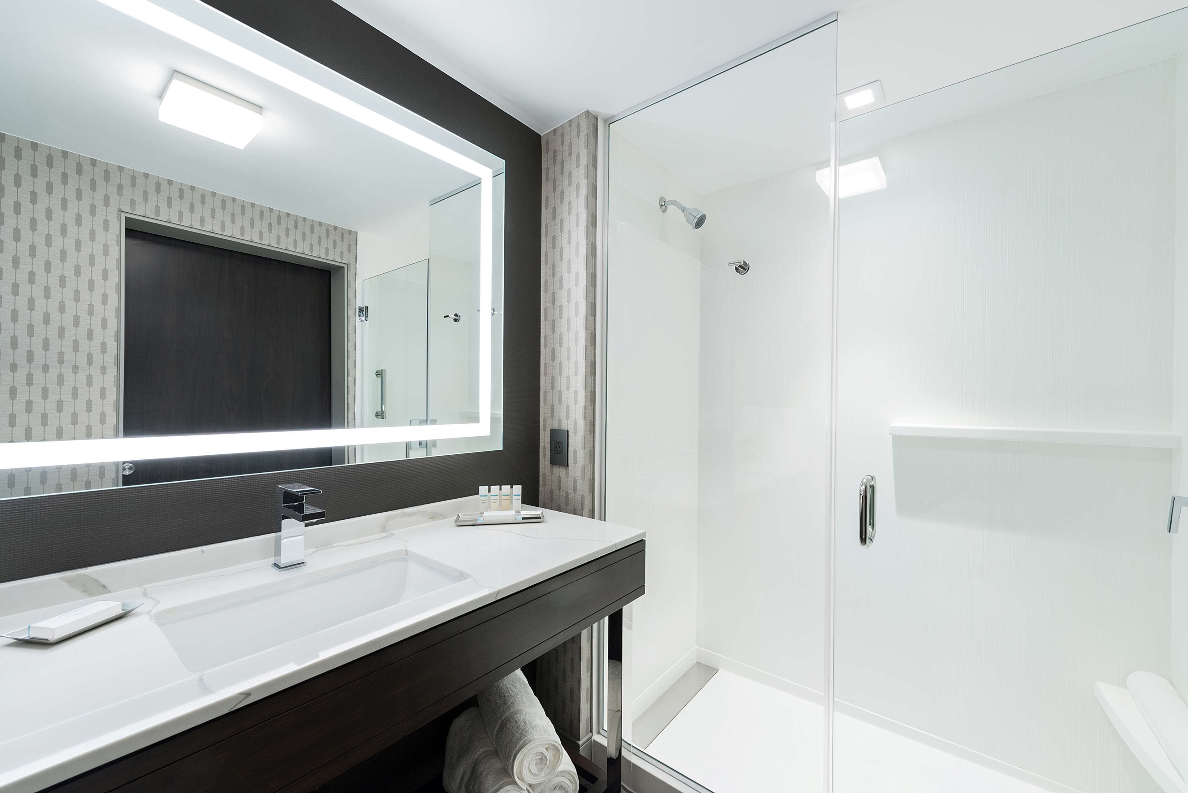 A modern bathroom with a large mirror, two sinks, and a glass-enclosed shower.