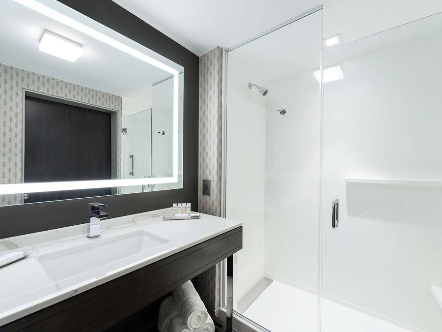 A modern bathroom with a large mirror, two sinks, and a glass-enclosed shower.