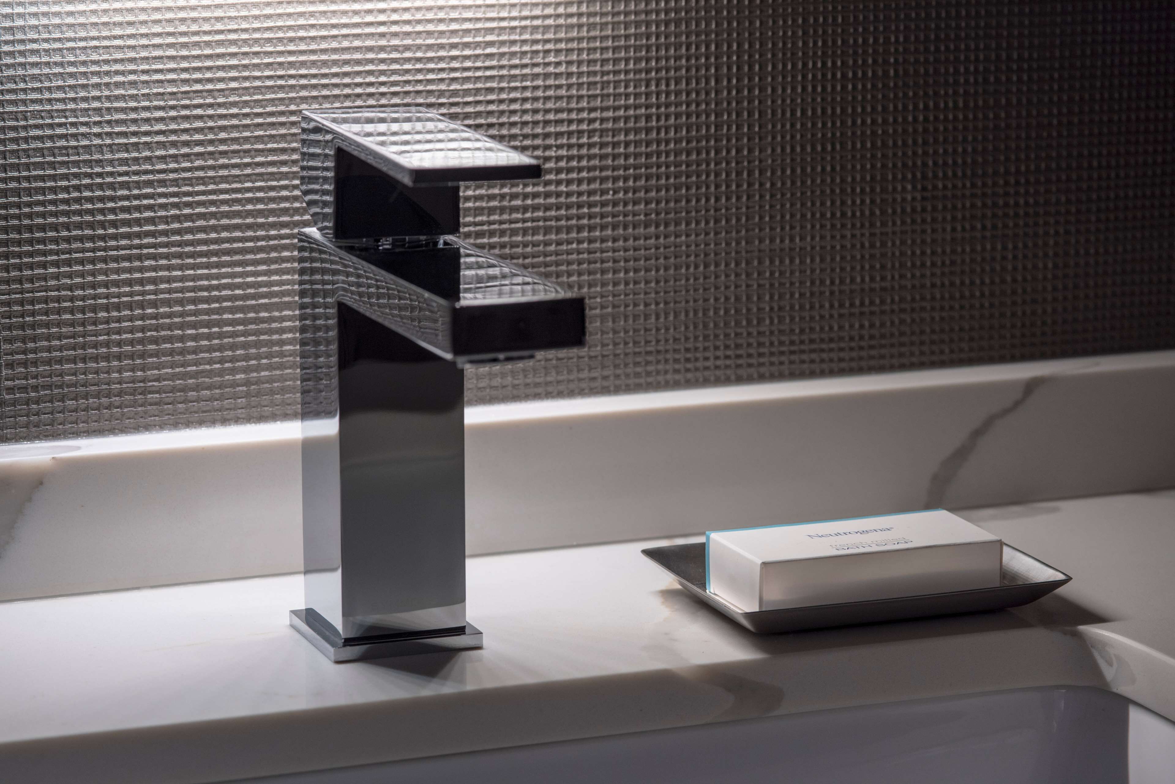 Un baño moderno con un grifo metálico elegante y una caja de artículos de tocador sobre el mostrador.