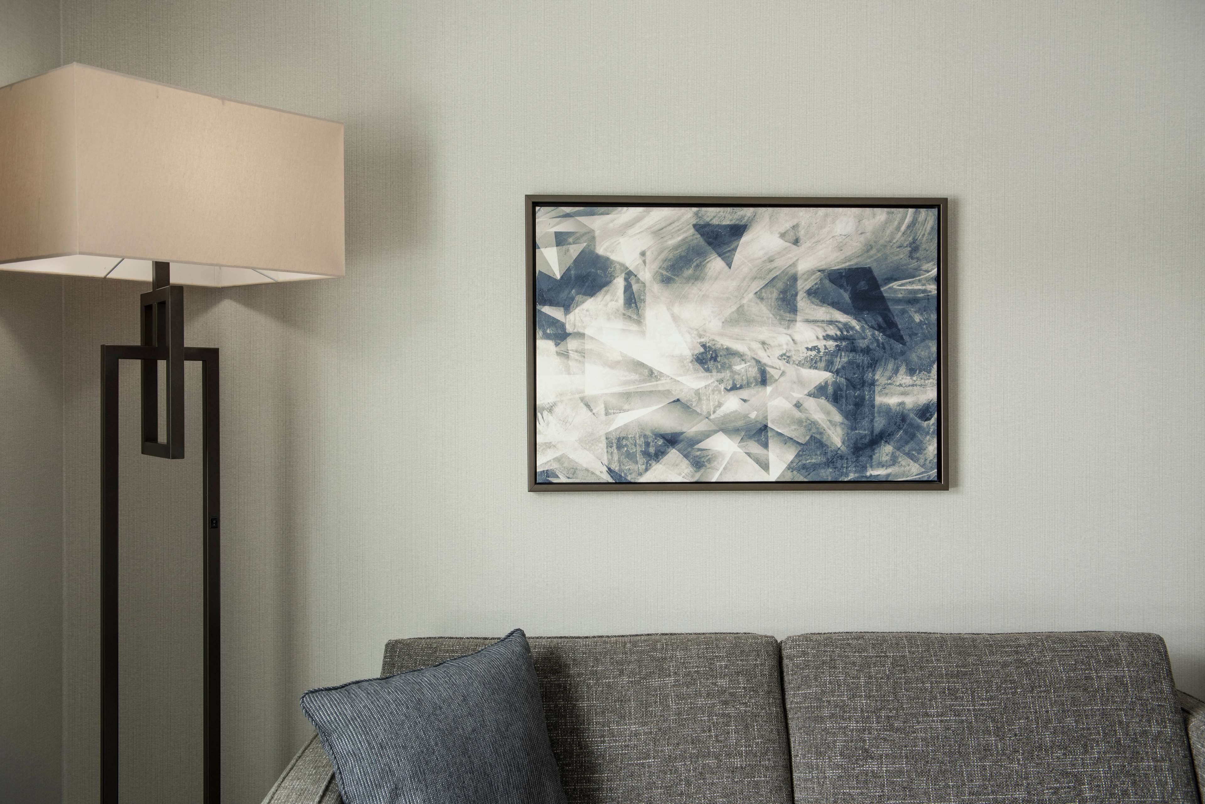 En moderne stue med en grå sofa, en gulvlampe og et indrammet abstrakt billede på væggen.