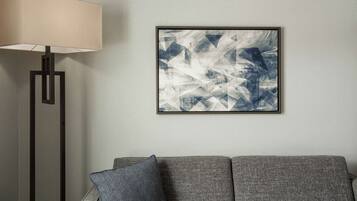 En moderne stue med en grå sofa, en gulvlampe og et indrammet abstrakt billede på væggen.