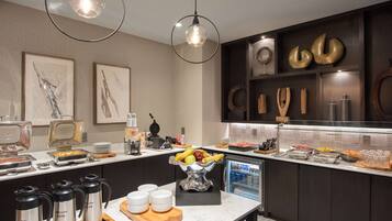 A modern kitchen with a marble countertop, coffee makers, a fruit bowl, and a refrigerator.