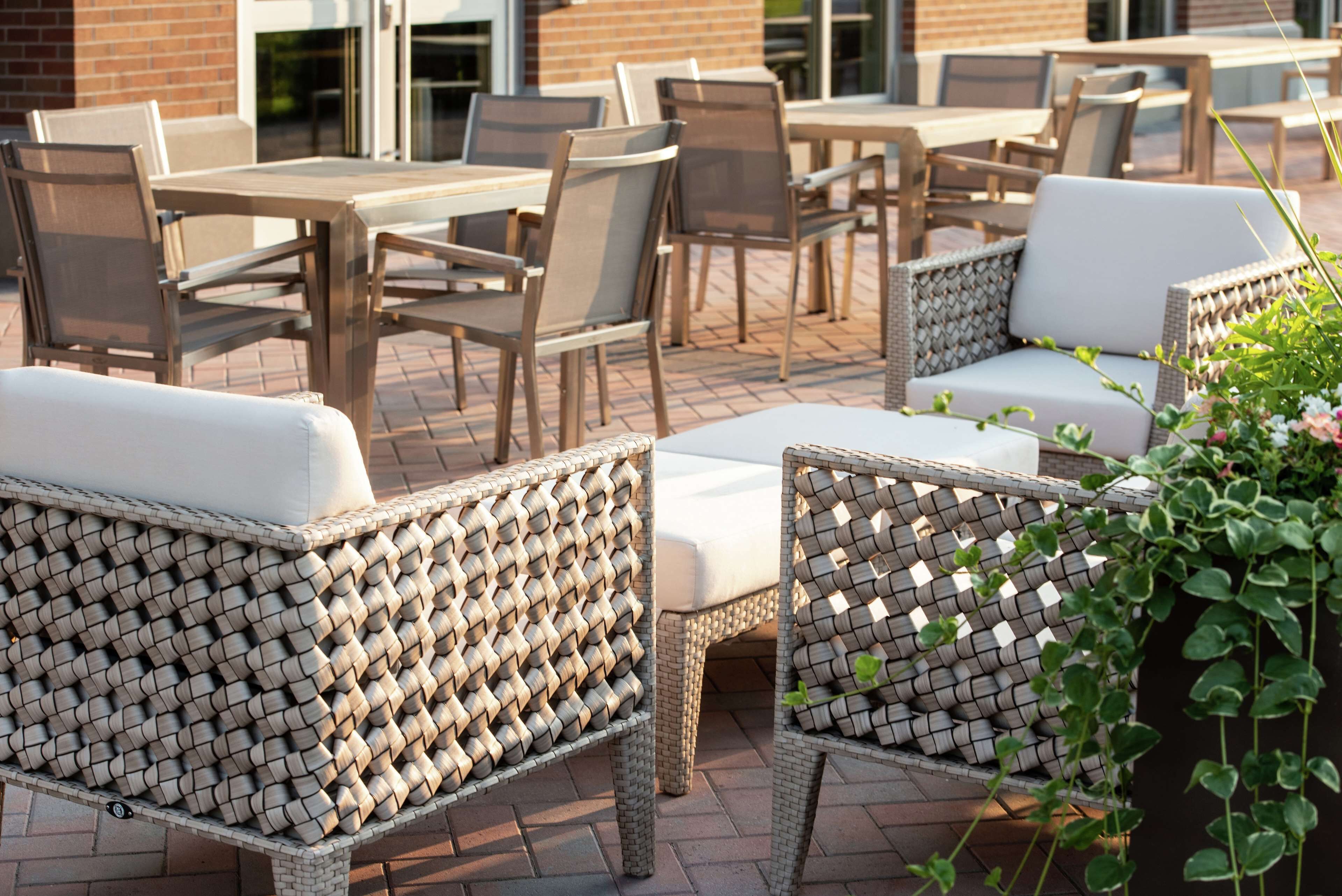 An outdoor seating area with wicker chairs and tables, a brick wall, and a building in the background.