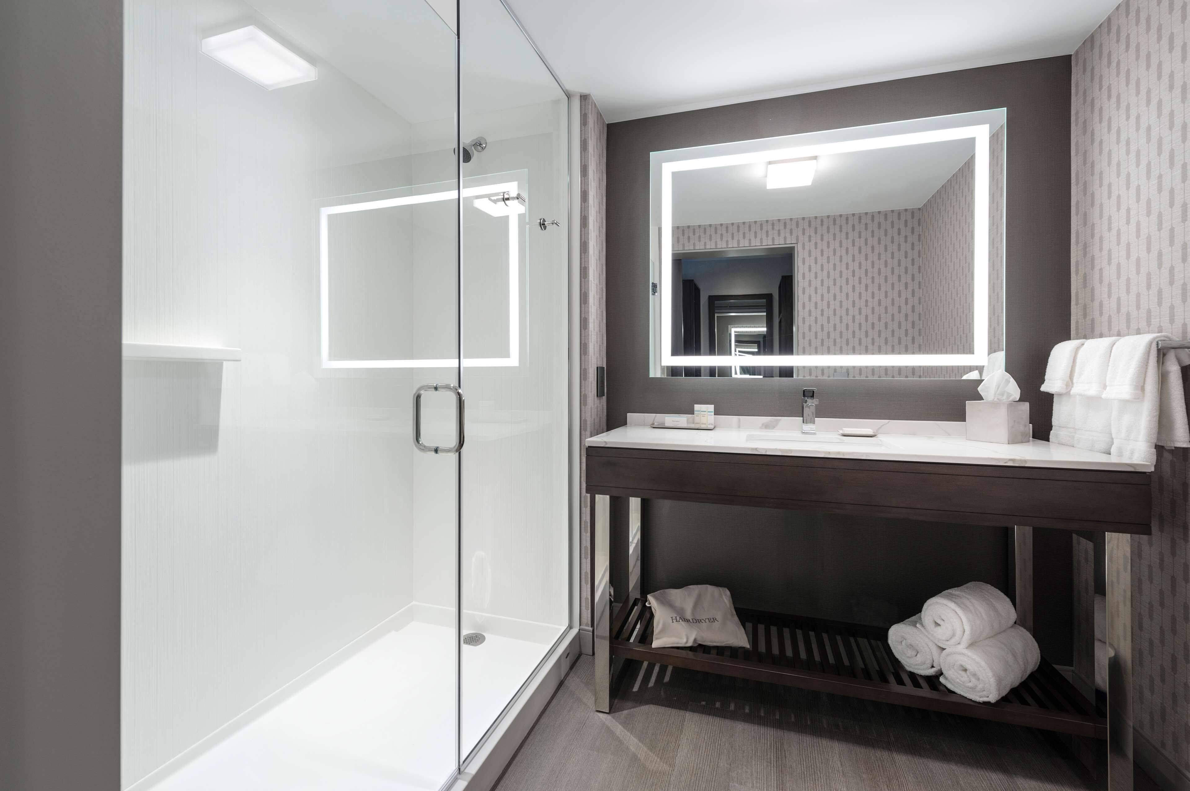 A modern bathroom with a glass shower enclosure, a vanity with a mirror, and neatly arranged towels.