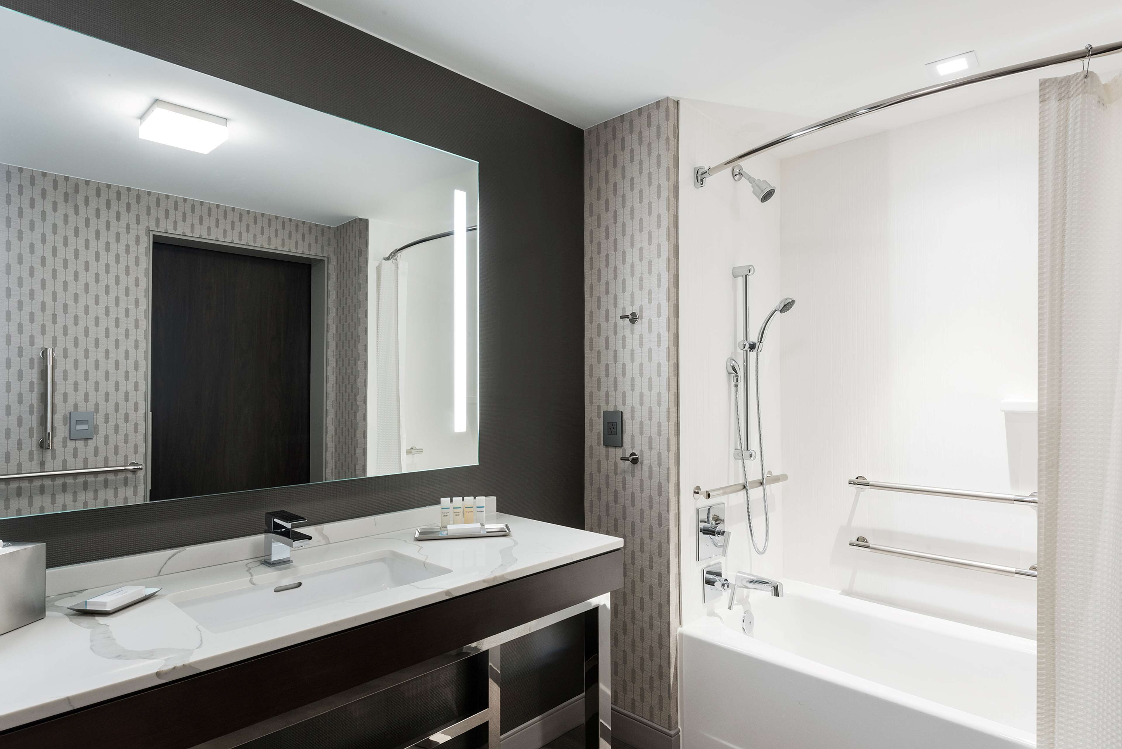A modern bathroom with a large mirror, two sinks, a bathtub, and a shower.