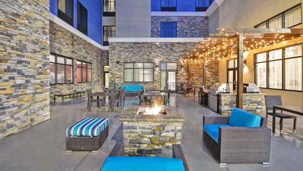 An outdoor patio with stone walls, wicker furniture, a fire feature, and string lights.